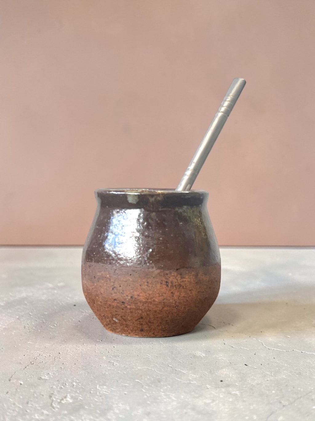 Mate caldera artesanal en gres color cobre oscuro con bombilla de acero, fondo rosa salmón. Matera Rob®
